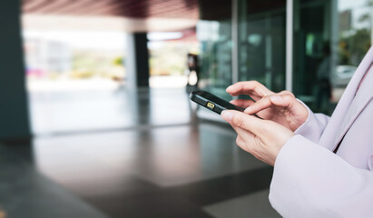 Businesswoman's hands using a smartphone against a glass background in an office. Social network concept