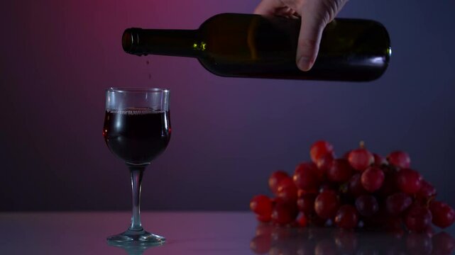 A man holds a glass of red wine for tasting, stands near the vineyard before sunset