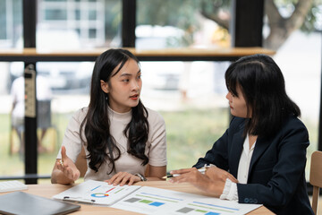 Two businesswomen are sitting at a table, analyzing charts and graphs, engaging in a productive...