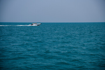 Fast motorboat racing across the rippling water surface, creating a white trail under the bright sun on a beautiful summer day
