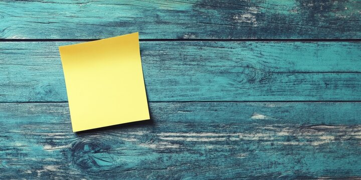 Yellow sticky note on an aged teal wooden surface, positioned center-left, ideal for reminders and messages with ample space for text.