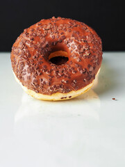 A chocolate donut with sprinkles on top. The donut is sitting on a white surface and dark...