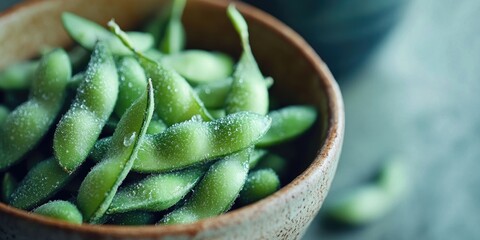 Freshly shelled edamame pods with a light dusting of salt, nestled in a rustic brown bowl, set against a soft green background.