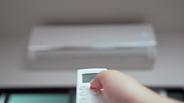 Close up of a hand holding an air conditioner remote pointing it towards to turn it on in a cozy living room at home. Hand using remote controller for adjust Air conditioner