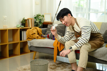 Man in an apron sitting in a cluttered living room and throwing crumpled paper into a trash