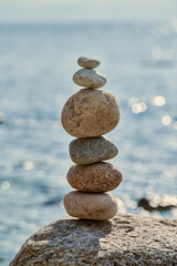 Stack of smooth stones precariously balanced on larger rock by calm seaside, symbolizes balance and serenity, evoking peaceful and meditative atmosphere