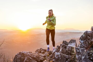 Obraz premium Woman running on rocky terrain at sunrise.
