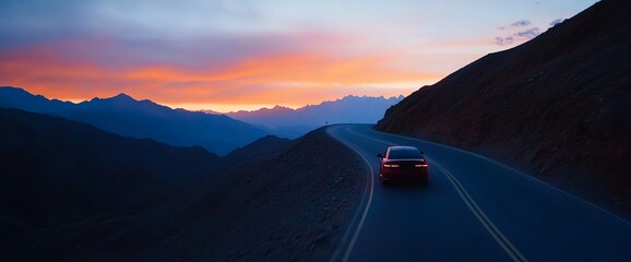 A lone vehicle journeys down a winding road at dusk, amidst the grandeur of mountain scenery
