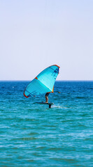 Wing Foil athlete gliding over the ocean waves with his wing covering part of his body to gain...