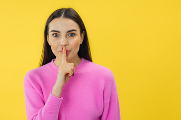 young attractive brunette woman with sincere emotions showing shh gesture. Keep secret isolated on yellow background