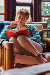 Obraz premium Mature woman sitting in a chair at home reading a book alone, enjoying a peaceful moment of relaxation and leisure in a quiet indoor environment with a cozy and comfortable atmosphere