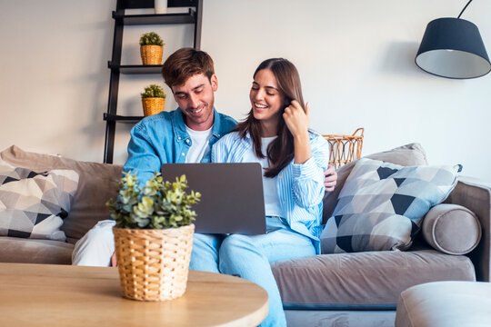 A young couple enjoys a relaxed afternoon at home using technology, watching a movie or series via streaming services on their laptop, and browsing social media for fun. Working on line with computer - Powered by Adobe