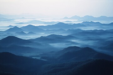 Fototapeta premium Endless rolling mountains blend into the horizon, covered in a veil of mist, creating a breathtaking and tranquil, mysterious vista.