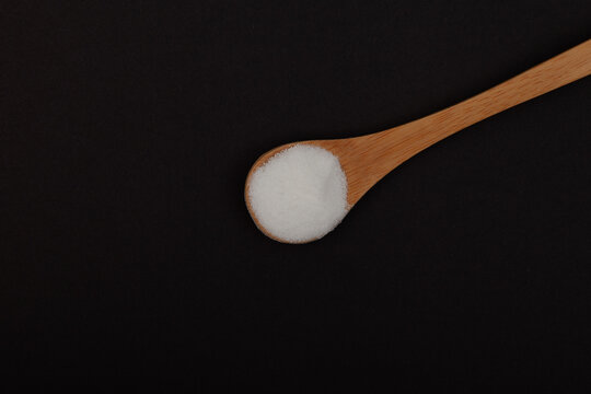 Food additive E575 in wooden spoon on dark background. Acidity regulator, baking powder. Glucono-delta-lactone, also known as gluconolactone. Pure GDL, white odorless crystalline powder