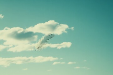 A single feather drifts gracefully against a backdrop of clear blue sky and cotton-like clouds.