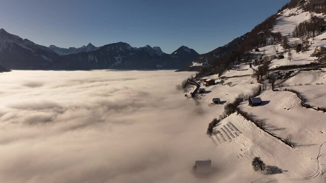 Aerial view of Amden, Switzerland, revealing a mesmerizing winter landscape where snow-covered slopes meet a dense sea of clouds. The contrast between the crisp alpine peaks and the misty valley below