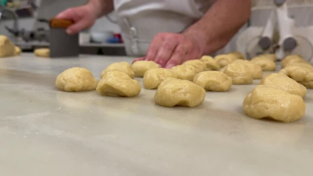 Closeup view of the hands of caucasian pastry chef preparing handmade pastry dough on a white color marble table inside a traditional workshop. 4K