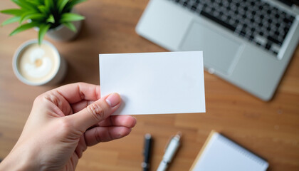 Obraz premium A close-up of a hand holding a blank business card over a desk background. The mockup highlights the card's clean and professional design, perfect for showcasing branding, contact information