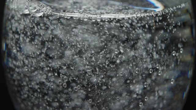 Close up of effervescent bubbles in sparkling water rising dynamically in a clear glass, slow motion