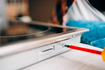 Close-up view of a technician skillfully using a screwdriver to repair a modern induction cooker hob, highlighting the intricate process involved in appliance maintenance and troubleshooting