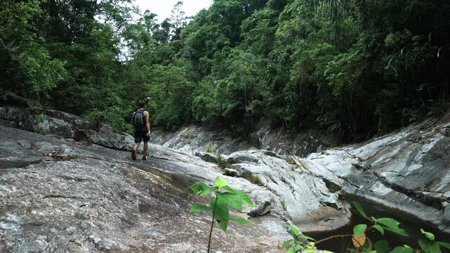 A tourist walks along the rocky bed of a mountain river in the tropics