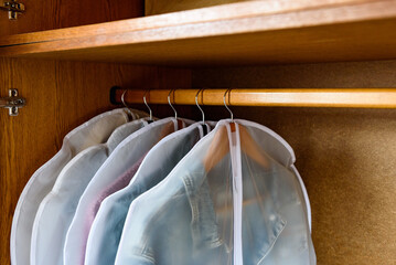 Clothes on hangers in white protective covers in wardrobe.