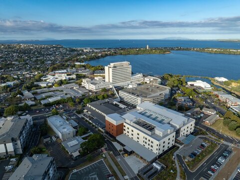 Aerial view of a modern hospital complex, nestled beside a harbor, with parking lots and surrounding residential areas. Cityscape, healthcare. NORTH SHERE HOSPITAL, AUCKLAND, NEW ZEALAND