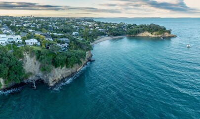 Fototapeta premium Coastal town with a secluded beach, a catamaran in the bay. Tranquil scene from above. CASTOR BAY, AUCKLAND, NEW ZEALAND