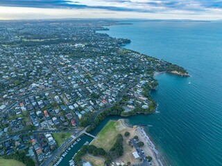 Aerial view of a coastal city, showing residential areas, a marina, and a beach. Suburban homes...