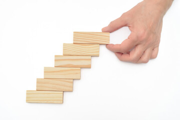 Hand of a businesswoman putting or removing wooden block on the top of wooden blocks stacked in the shape of stairs on the white background. Concept of strategy and solution in business.