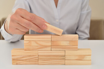 Hand of a businesswoman putting or removing wooden block on the top of wooden pyramid shape on the...
