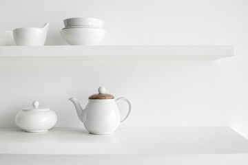 Fototapeta premium The concept of a stylish modern kitchen is illustrated by kitchenware utensils such as mugs, cups, a teapot, and a tray, which are placed on a shelf set against a white background and accompanied by