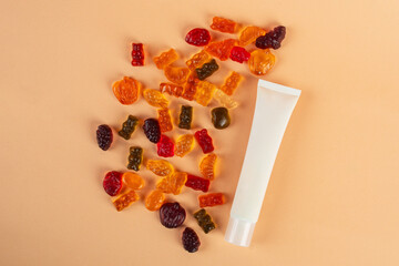 Plastic white tube for cream or lotion. Skin care or sunscreen cosmetic with stylish props and fruit gummi on cream background.