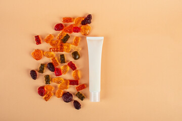 Plastic white tube for cream or lotion. Skin care or sunscreen cosmetic with stylish props and fruit gummi on cream background.