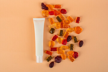 Plastic white tube for cream or lotion. Skin care or sunscreen cosmetic with stylish props and fruit gummi on cream background.