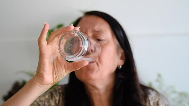 Middle age woman drinking water with vitamin C and doing faces because of the bad flavour.