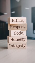 wooden blocks stacked vertically on a light surface display "ETHICS," "RESPECT," "CODE," "HONESTY," and "INTEGRITY" in dark brown font. A blurred office background emphasizes ethical business values