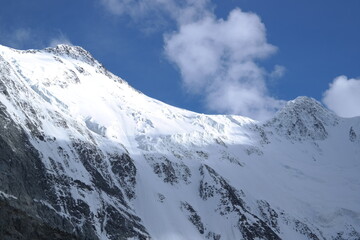 A stunning rock formation covered in snow, set against a clear blue sky with fluffy clouds in the...