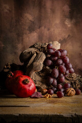 Bunch of red grapes on vine trunk on wooden table with pomegranates, vertical with copy space