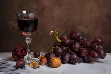 View of bunch of grapes with nuts and glass of red wine on marble, horizontal with copy space