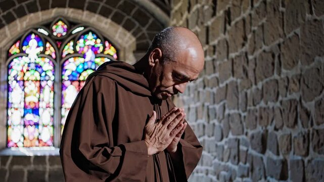 A monk in prayer, side view, in a stone chapel with stained glass. The video captures a serene, contemplative atmosphere with a low-angle shot.