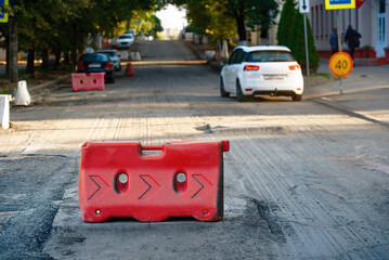 Red traffic barrier on gravel patched road, white car leaving, and speed limit sign. Red traffic...