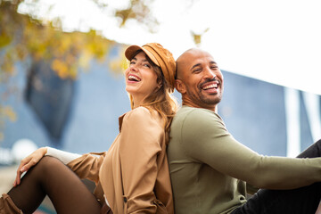 smiling couple sitting back to back outdoors