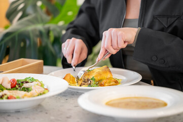 A person is enjoying a delicious meal, using a fork and knife to slice into a savory dish. Plates of salad and soup are visible in a cozy dining setting.