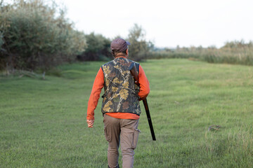 Mature hunter man holding a shotgun and walking through a field