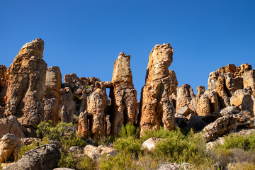 Towering sandstone rock formations with deep orange hues stand against a vivid blue sky, creating a striking contrast in a remote wilderness.
