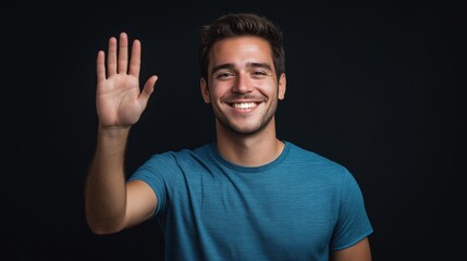 A smiling man in a blue T-shirt waving his hand at the camera against a black background. Presenting. Bussinessman. Ideas