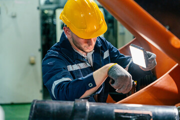 Worker performs maintenance tasks in industrial setting using a portable light to inspect machinery...