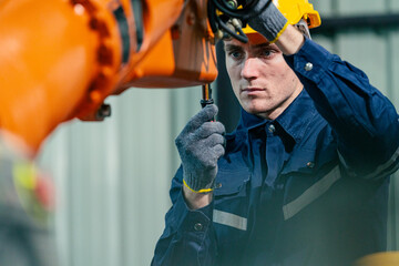 Young technician repairs an industrial robotic arm in a manufacturing facility