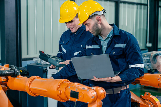 Engineers conducting maintenance check on robotic arms in a manufacturing facility during daytime